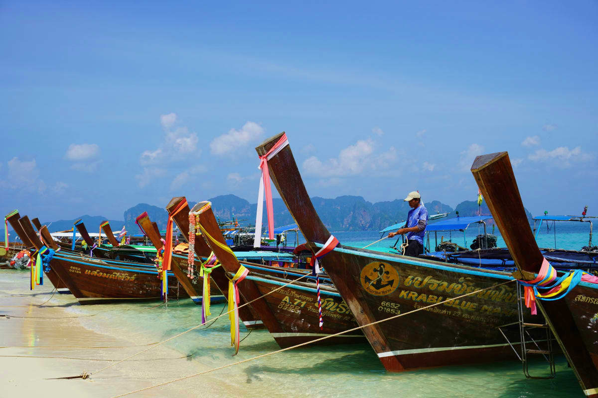 Krabi Island Tour from Phuket Traditional wooden longtail boats with colorful ribbons moored in turquoise water near Krabi islands with limestone cliffs in