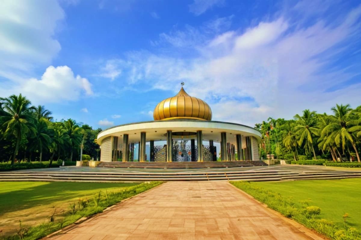 Modern circular building with golden dome surrounded by palm trees and manicured lawns in Kuala Lumpur