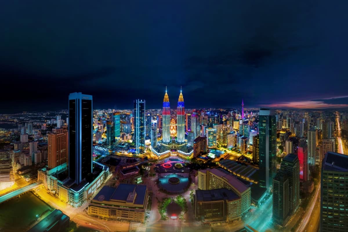 Kuala Lumpur City Discovery Tour Aerial night view of Kuala Lumpur skyline featuring illuminated Petronas Twin Towers with colorful lights and surrounding cit