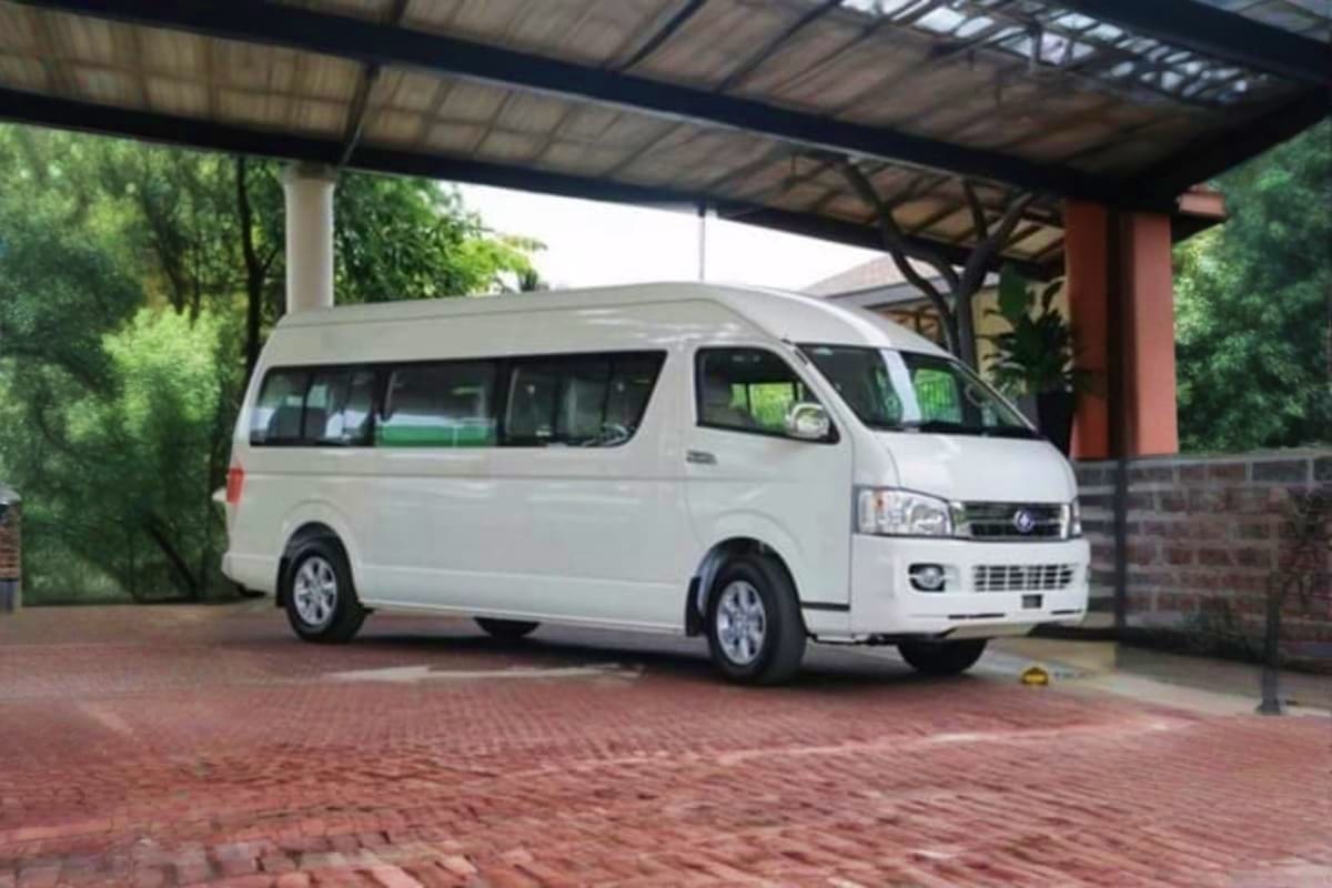 Private Vehicle Half Day With Driver White passenger van parked under covered carport with brick paving and landscaped surroundings