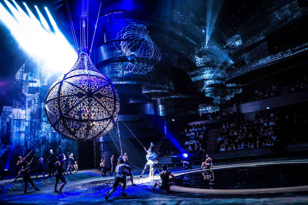 La Perle by Dragone Dubai Futuristic circus performance inside La Perle theater with acrobats, illuminated wire sphere prop, and blue stage lighting in