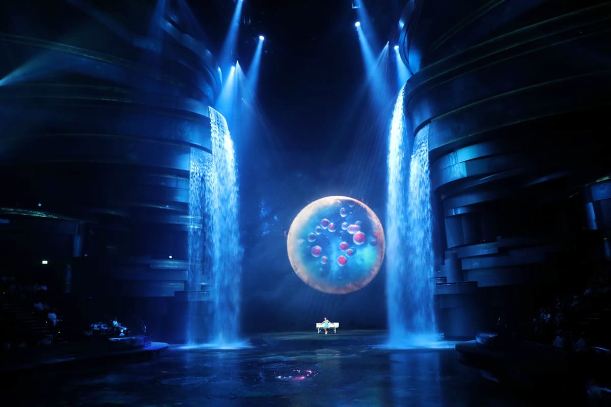 La Perle by Dragone Dubai Illuminated jellyfish projection floating above a grand piano on stage with blue light beams in La Perle theater Dubai