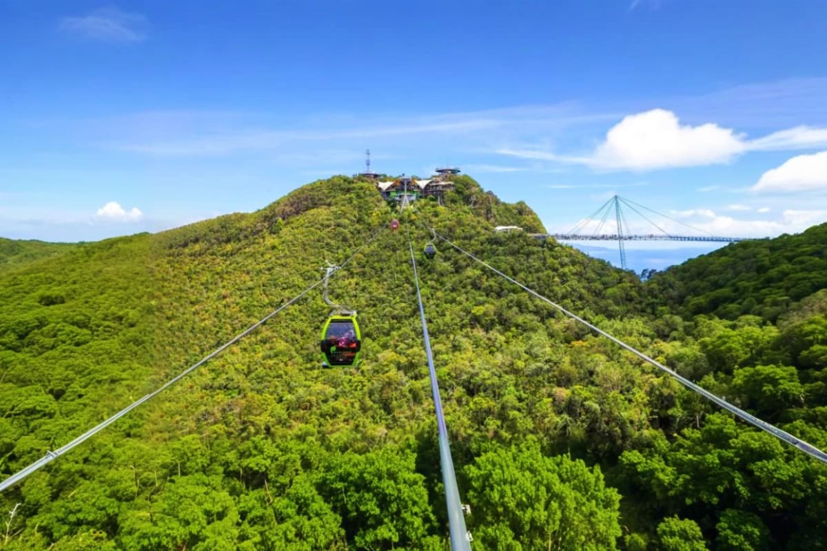 Langkawi Cable Car Langkawi Cable Car ascending green forested mountain peak with suspension bridge visible in distant background under blue sky