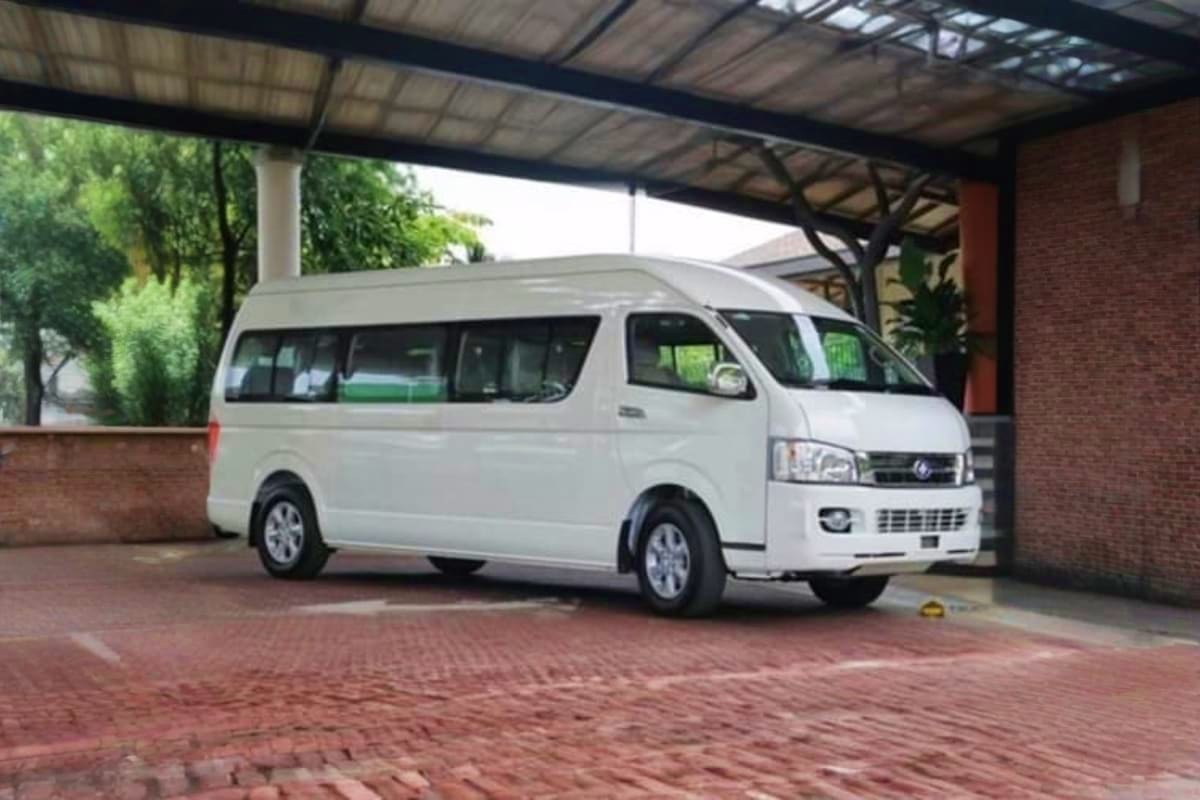 White passenger van parked under covered carport with brick building and green foliage in background