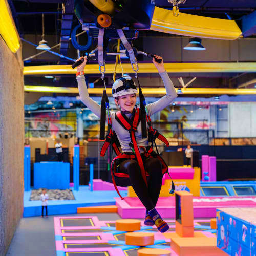 Loco Bear Entertainment Hub Child wearing safety harness flying on zipline course in colorful indoor adventure park with foam obstacles and neon lighting