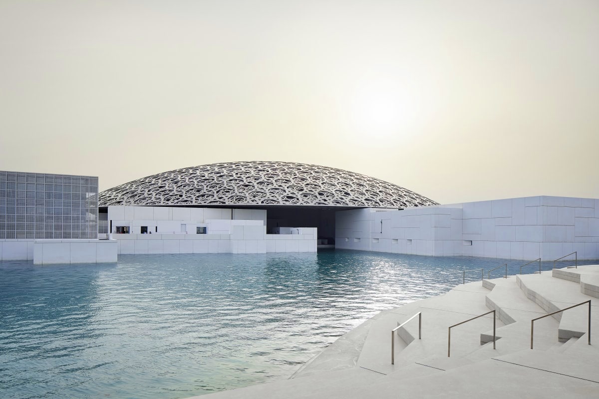 Louvre Abu Dhabi museum with distinctive white dome and geometric lattice roof overlooking waterfront promenade