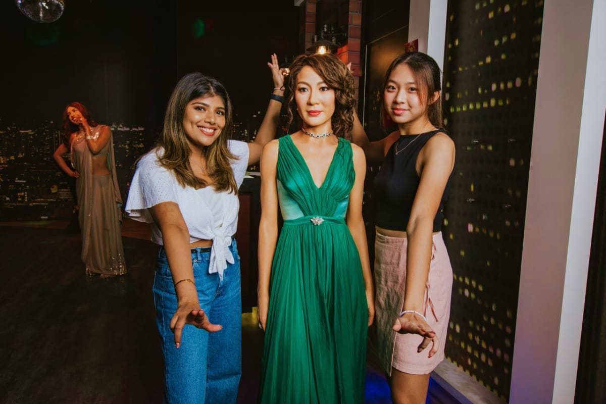 Three young women posing together at Madame Tussauds Singapore with city skyline and wax figures visible in background