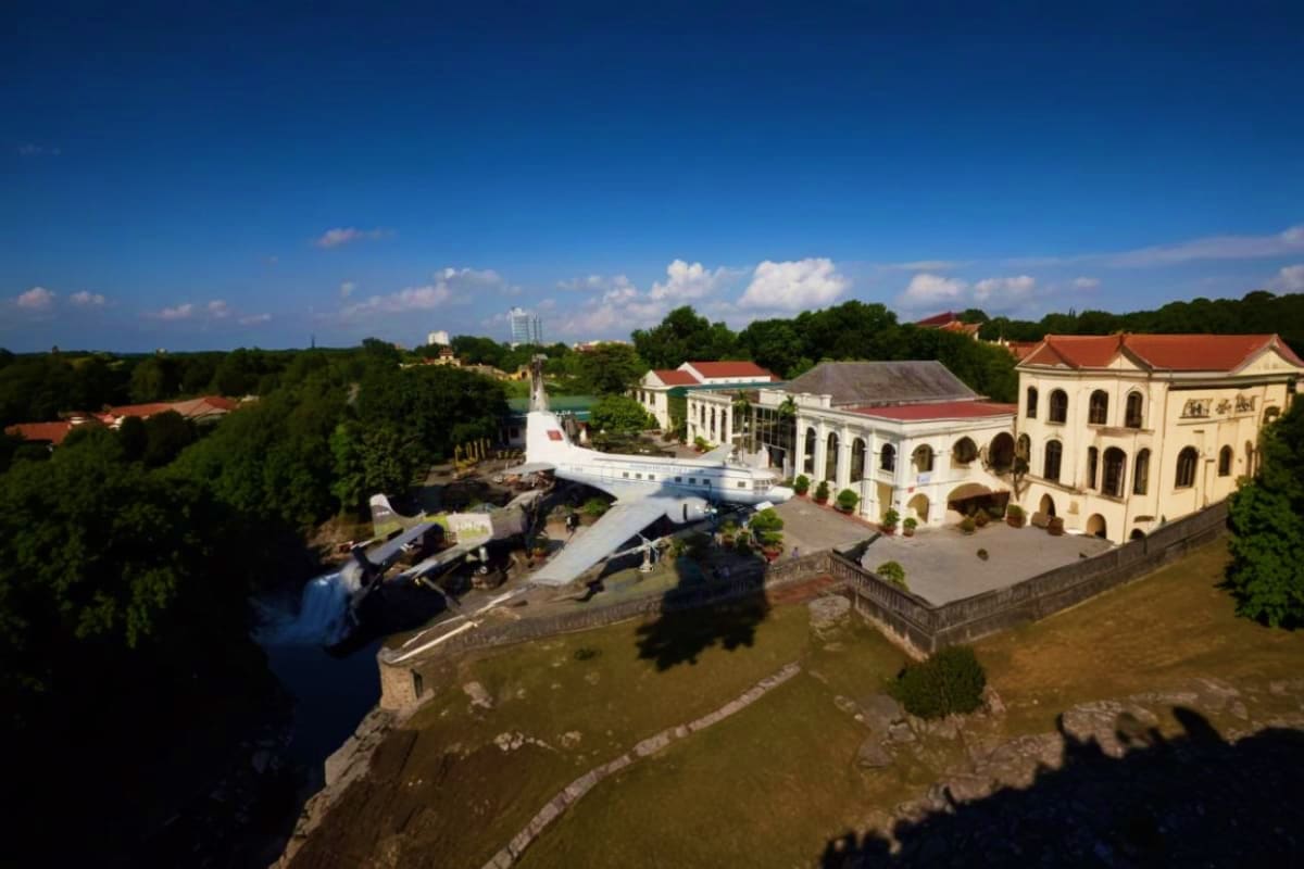 Aerial view of a decommissioned aircraft displayed at a military museum complex beside a river, with colonial architecture bu