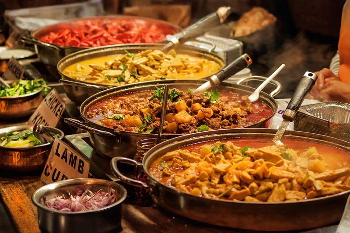 Buffet spread with multiple steel pots of Indian curries, lamb dishes, and rice served at a restaurant in Dubai Marina
