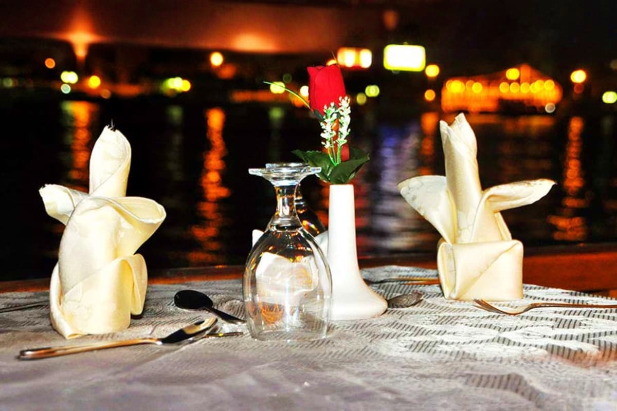 Elegant waterfront dinner table setting at Dubai Marina with white napkin folding, wine glass, and fresh flowers against nigh