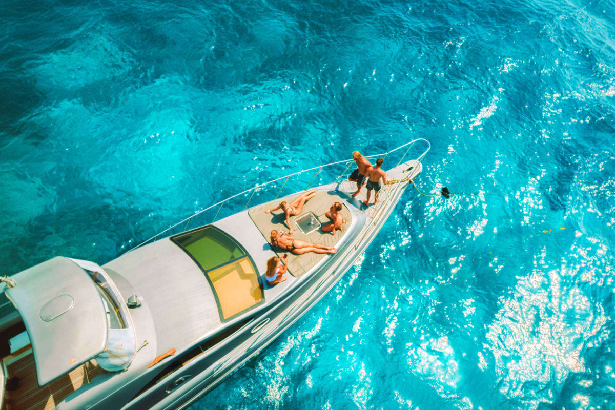 Aerial view of a white speedboat with passengers sunbathing on deck in clear turquoise ocean water