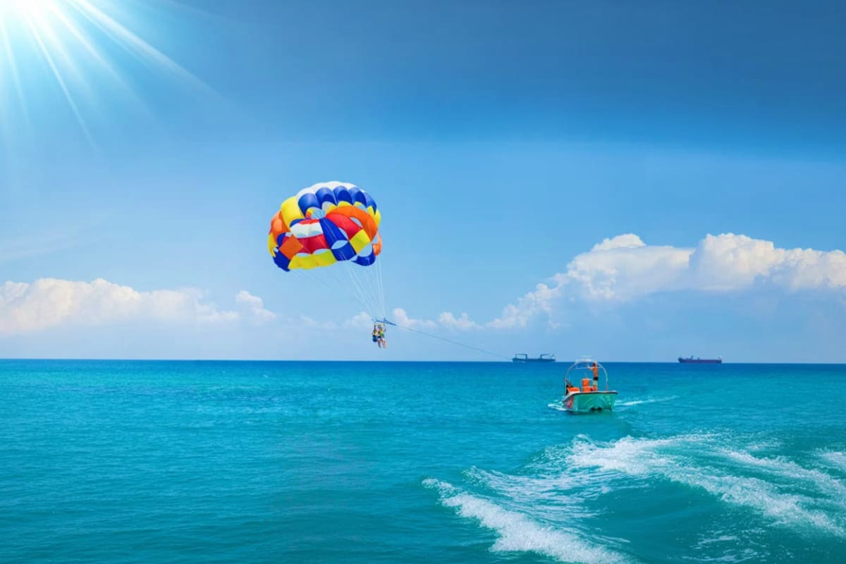 Person parasailing with colorful parachute over turquoise ocean waters at Cenang Beach with boat below