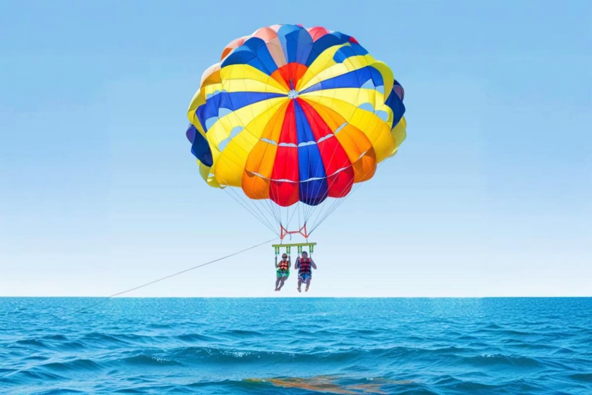 Two people parasailing with colorful parachute over blue ocean water at Cenang Beach
