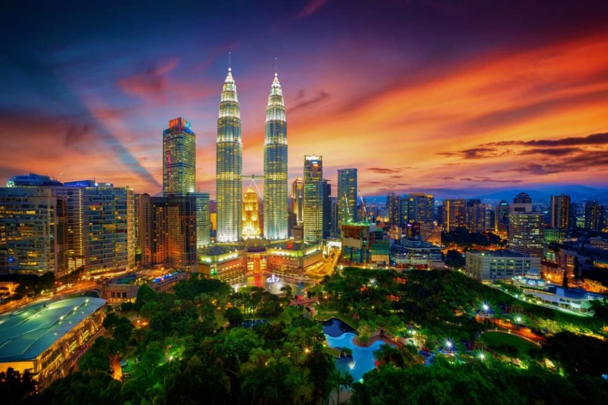 Petronas Twin Towers Kuala Lumpur Kuala Lumpur skyline at sunset with illuminated Petronas Twin Towers, surrounding skyscrapers, and green park area below