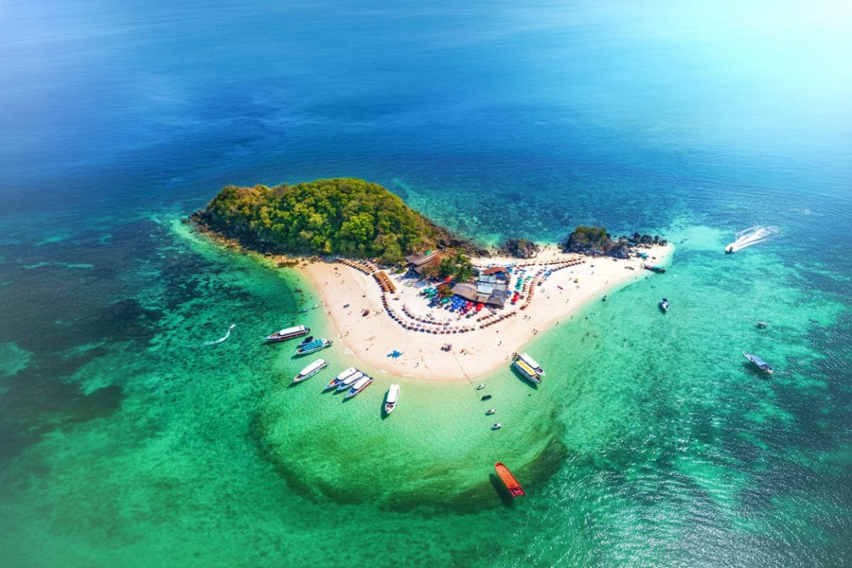 Phi Phi Island Bamboo Island Maya Bay and Pileh Lagoon by Speed Boat Aerial view of a tropical island with white sand beach, turquoise water, moored speedboats, and dense green vegetation, surro