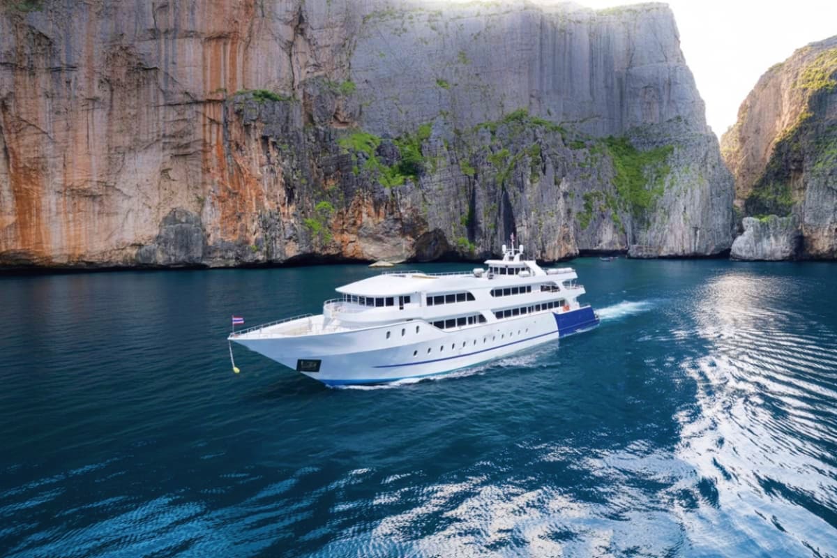 Large white and blue cruise ship anchored in turquoise waters surrounded by tall limestone cliffs at Phi Phi Island, Thailand