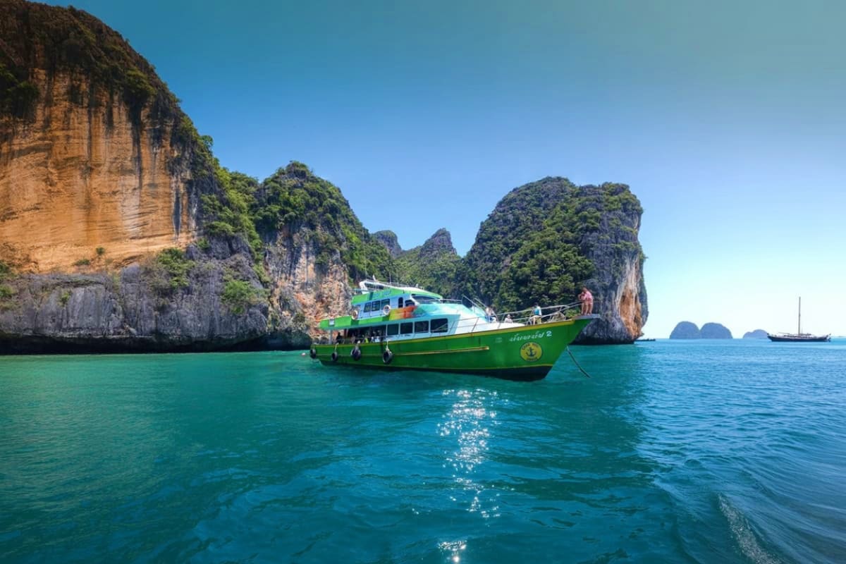 Green and white tour boat anchored in turquoise water between dramatic limestone cliffs at Phi Phi Islands Thailand