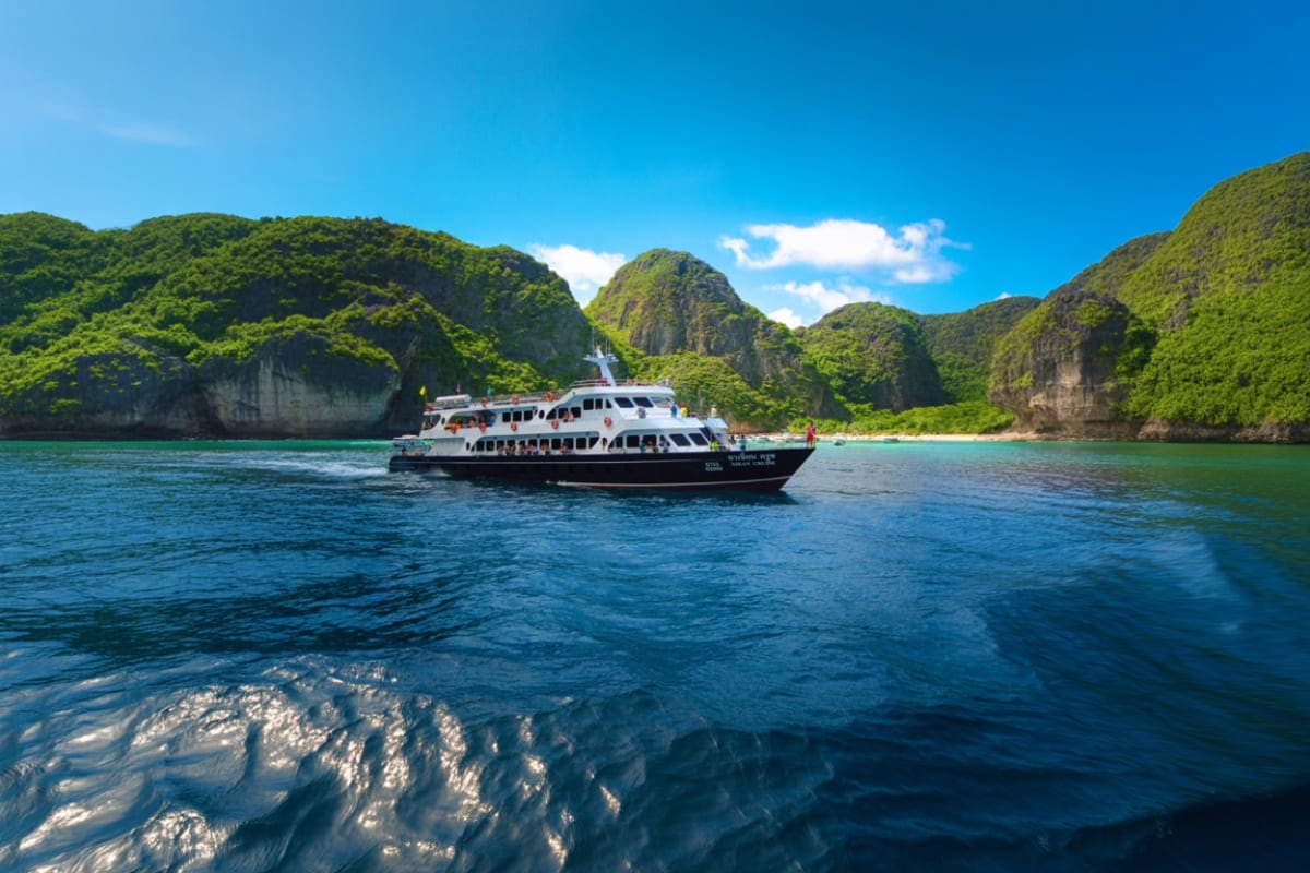 Tour boat anchored in turquoise water with steep limestone cliffs and lush green vegetation in Phi Phi Island bay