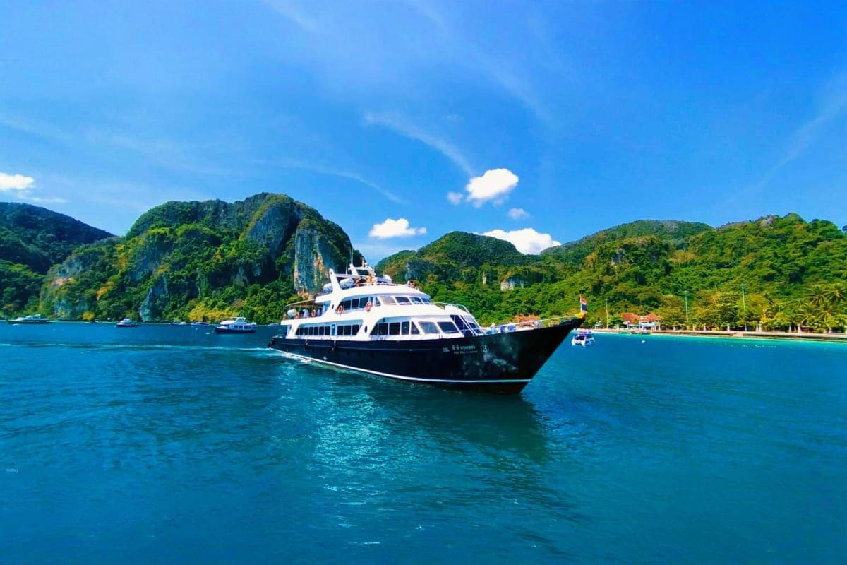 Luxury yacht anchored in turquoise waters off Phi Phi Island with lush green limestone cliffs and tropical beach in backgroun