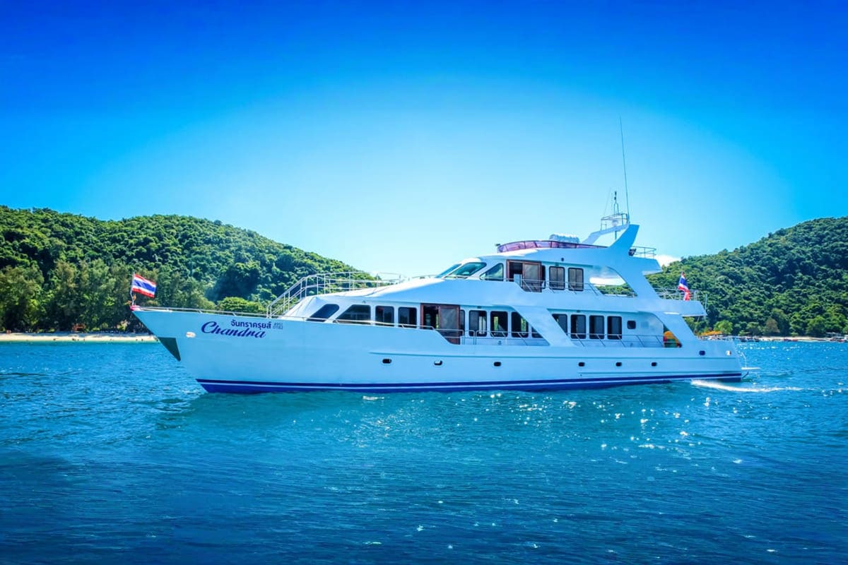 Blue and white luxury yacht anchored in turquoise water with forested hills in background under clear sky