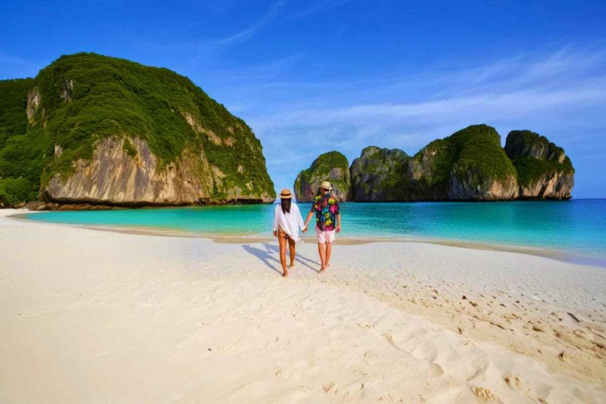 Couple holding hands on white sand beach with turquoise water and limestone cliffs of Phi Phi Islands in background