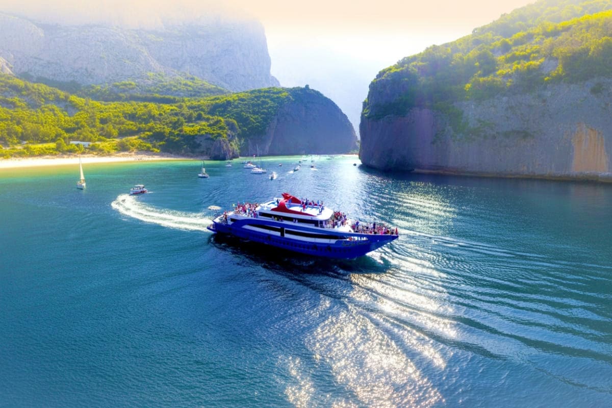 Blue catamaran with tourists anchored in turquoise waters near towering limestone cliffs and sandy beach at Phi Phi Islands T