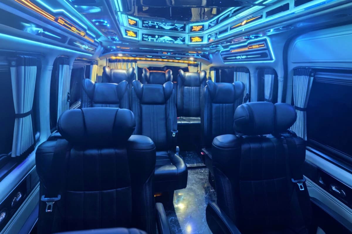 Luxury minibus interior with blue leather seats, neon lighting, and white curtains for airport transfer service