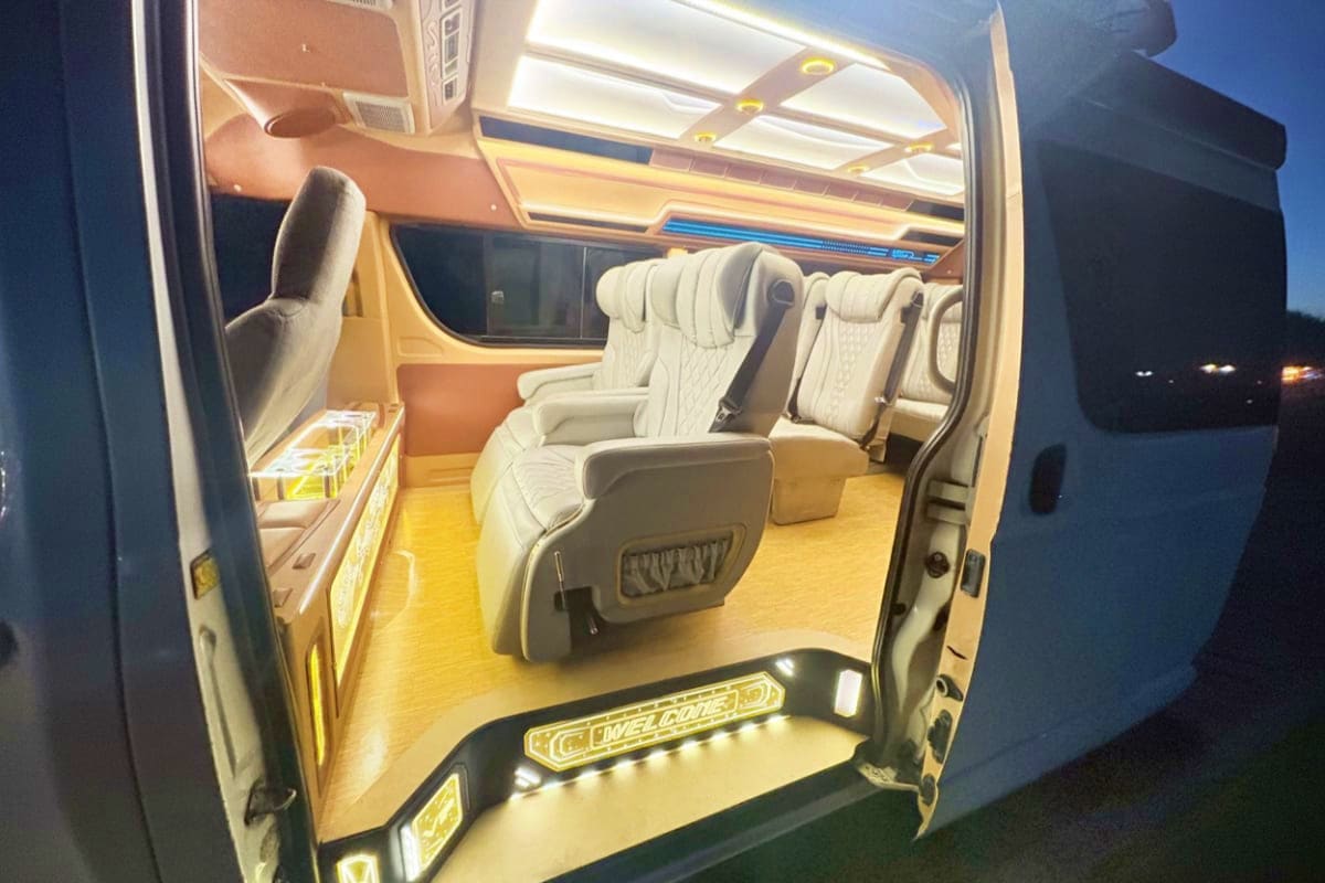 Interior of luxury van with cream leather seats, ambient yellow lighting, and panoramic roof for airport transfer service