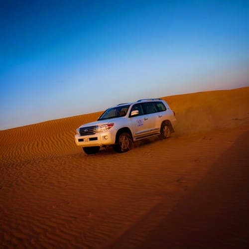White SUV parked on golden sand dunes under clear blue sky during desert safari