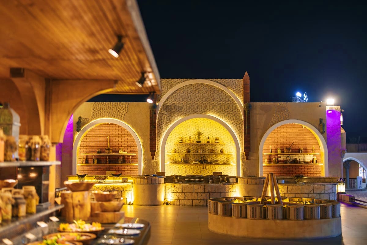 Illuminated traditional clay ovens at night in a desert courtyard with arched brick openings and warm golden lighting