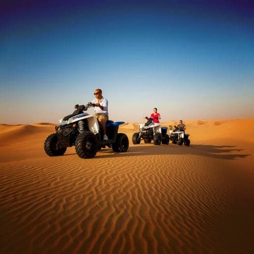 Group of tourists riding quad bikes across golden sand dunes in desert landscape during daytime