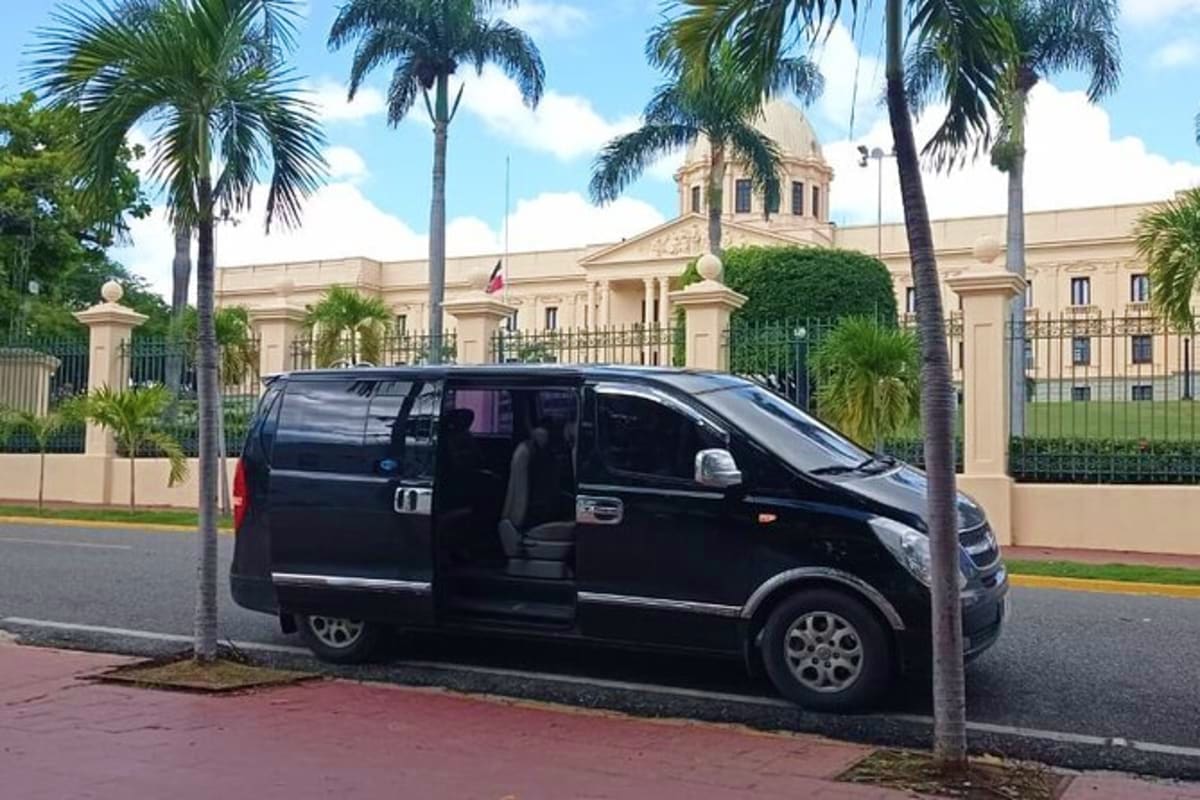 Black minivan parked on street with palm trees and beige colonial-style government building with dome in background
