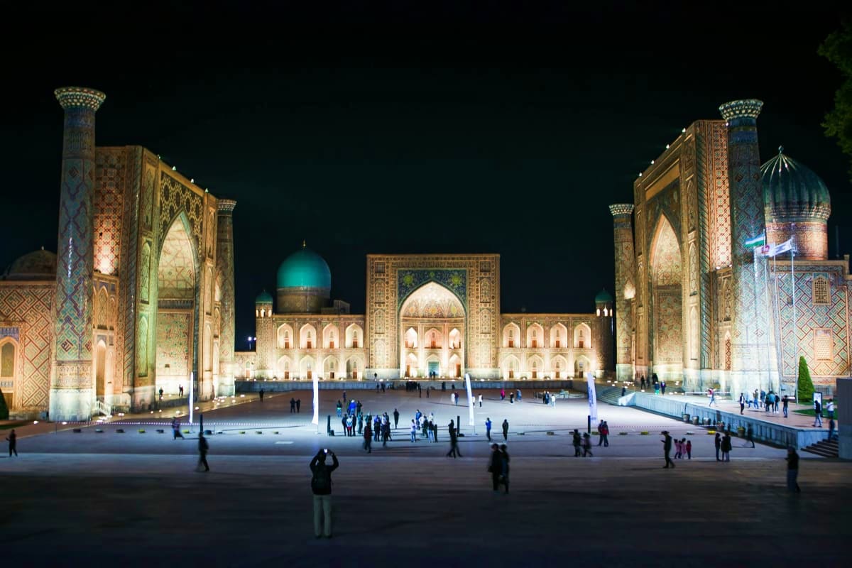 Registan Square in Samarkand illuminated at night with three ornate madrasahs featuring turquoise domes and intricate tile wo
