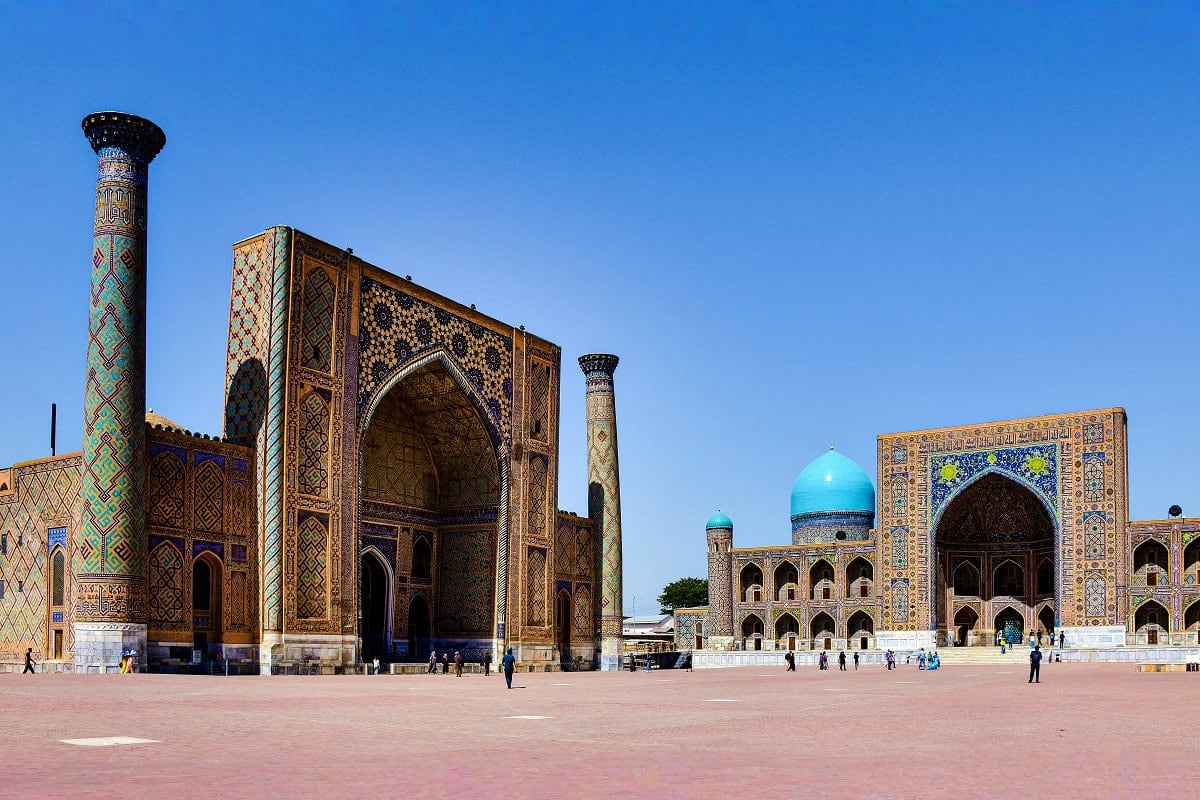 Registan square in Samarkand featuring three ornate madrasahs with turquoise domes, intricate tile work, and minarets under c