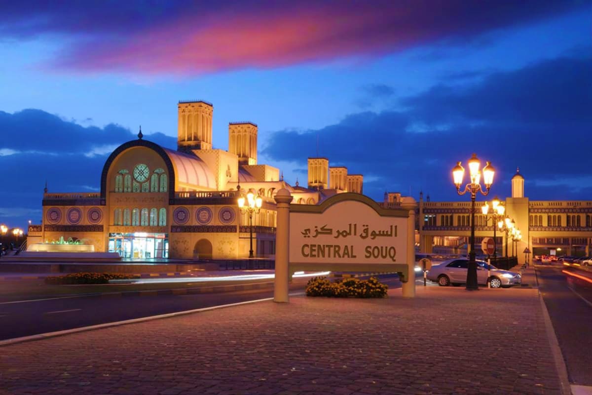 Central Souq entrance sign illuminated at dusk with traditional Islamic architecture and minaret towers in Sharjah at twiligh