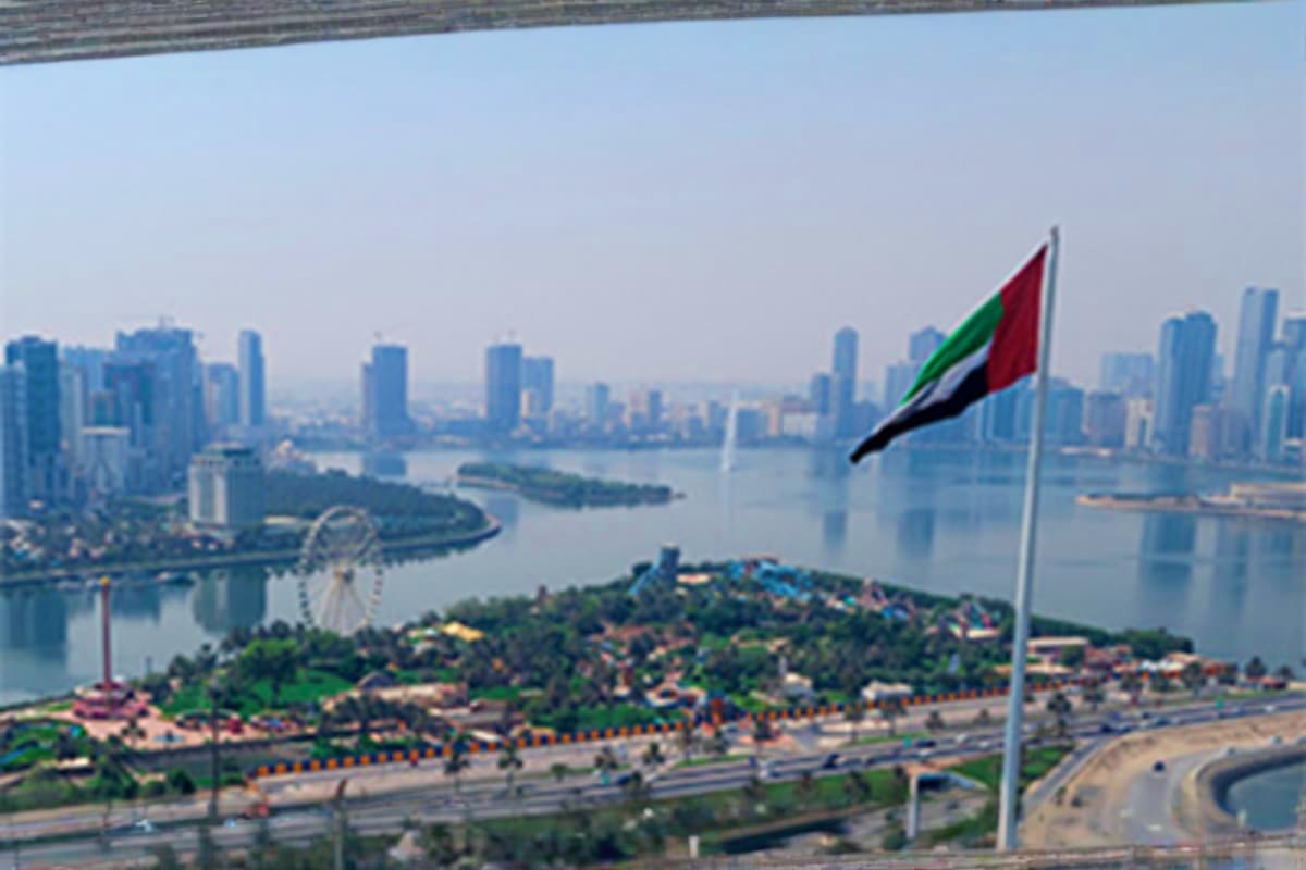 Aerial view of Dubai skyline with Sharjah waterfront, UAE flag, and theme park visible from elevated vantage point