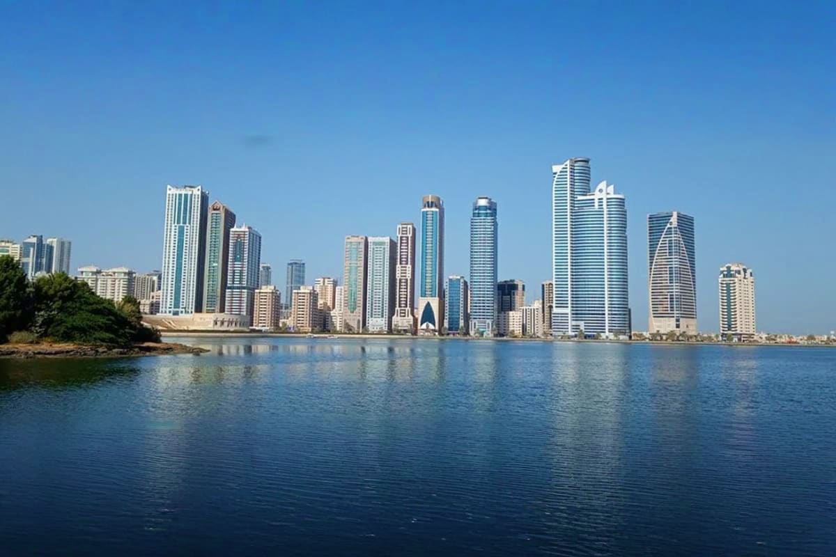 Skyline of modern high-rise buildings and skyscrapers reflecting in calm blue water under clear sky