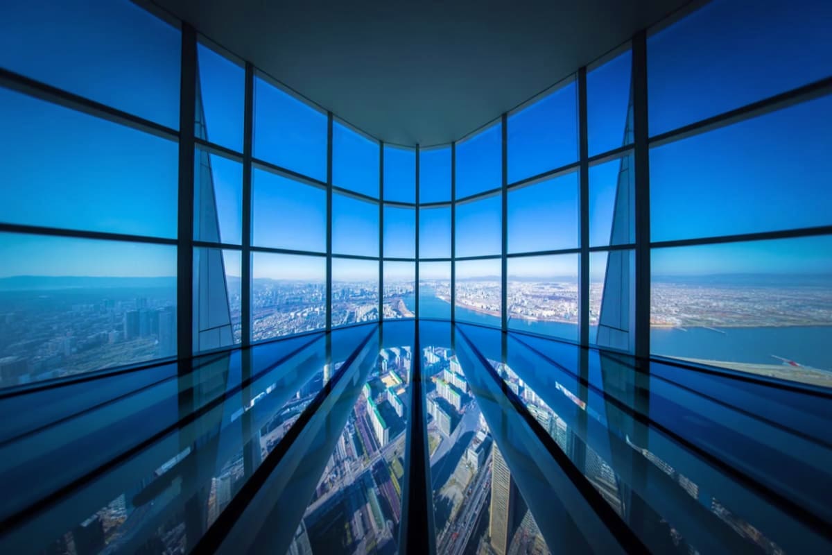 View from high-rise observation deck looking down at cityscape with buildings, waterfront, and clear blue sky