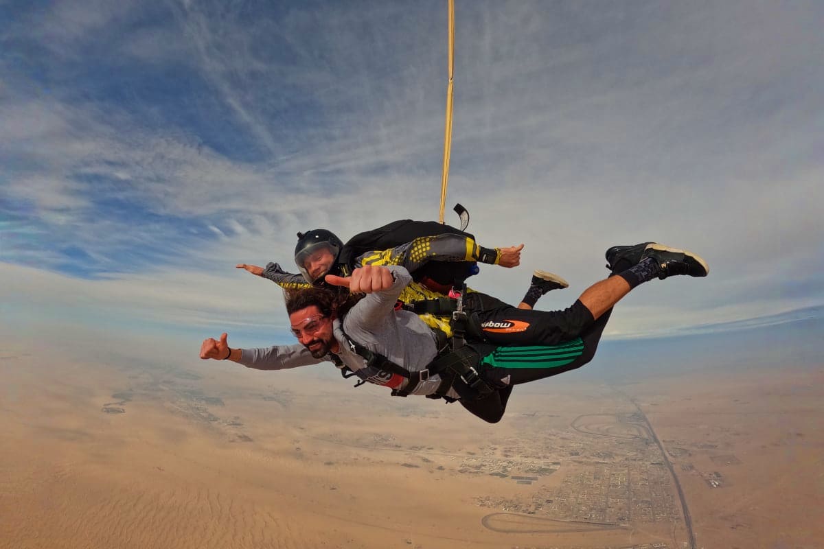 Tandem skydiving pair freefalling above Dubai desert landscape with Palm Jumeirah visible below