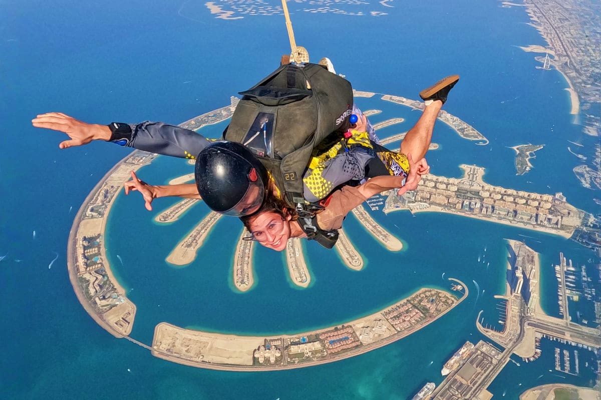 Skydiver in freefall above Palm Jumeirah with arms outstretched, showing the distinctive palm-shaped island and Dubai coastli