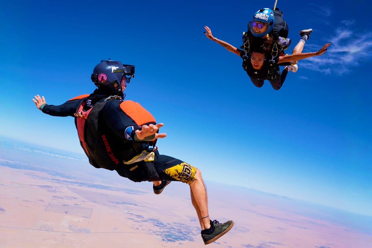 Skydiver and instructor in freefall over Dubai landscape with clear blue sky and desert terrain below