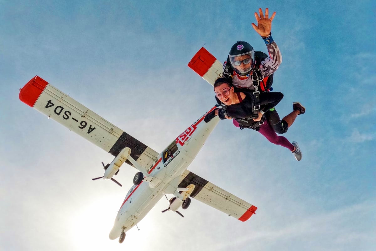 Skydiver and instructor exiting small aircraft during tandem skydiving jump against clear blue sky