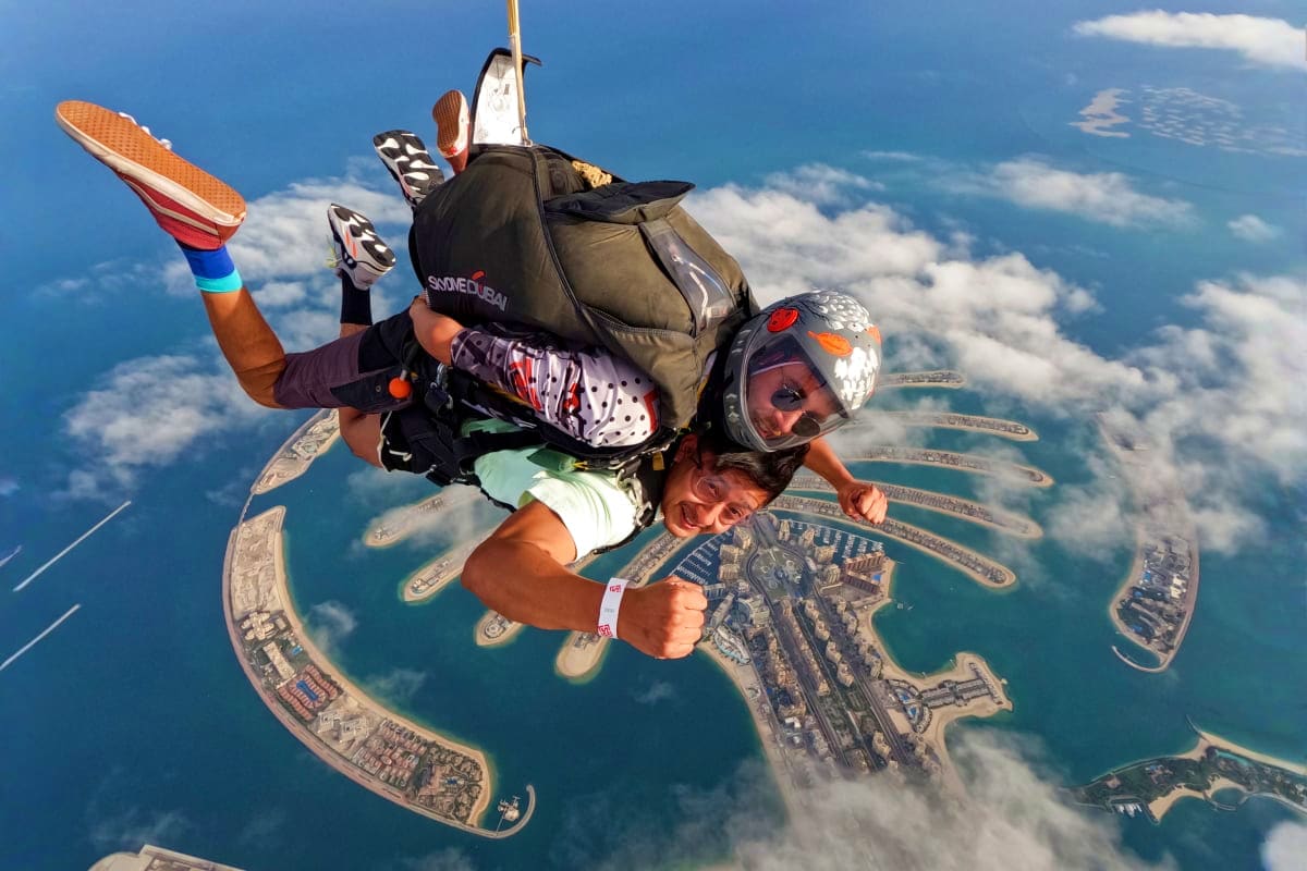Skydiver in freefall above Palm Jumeirah with tandem instructor, showing Dubai's iconic palm-shaped islands and turquoise wat