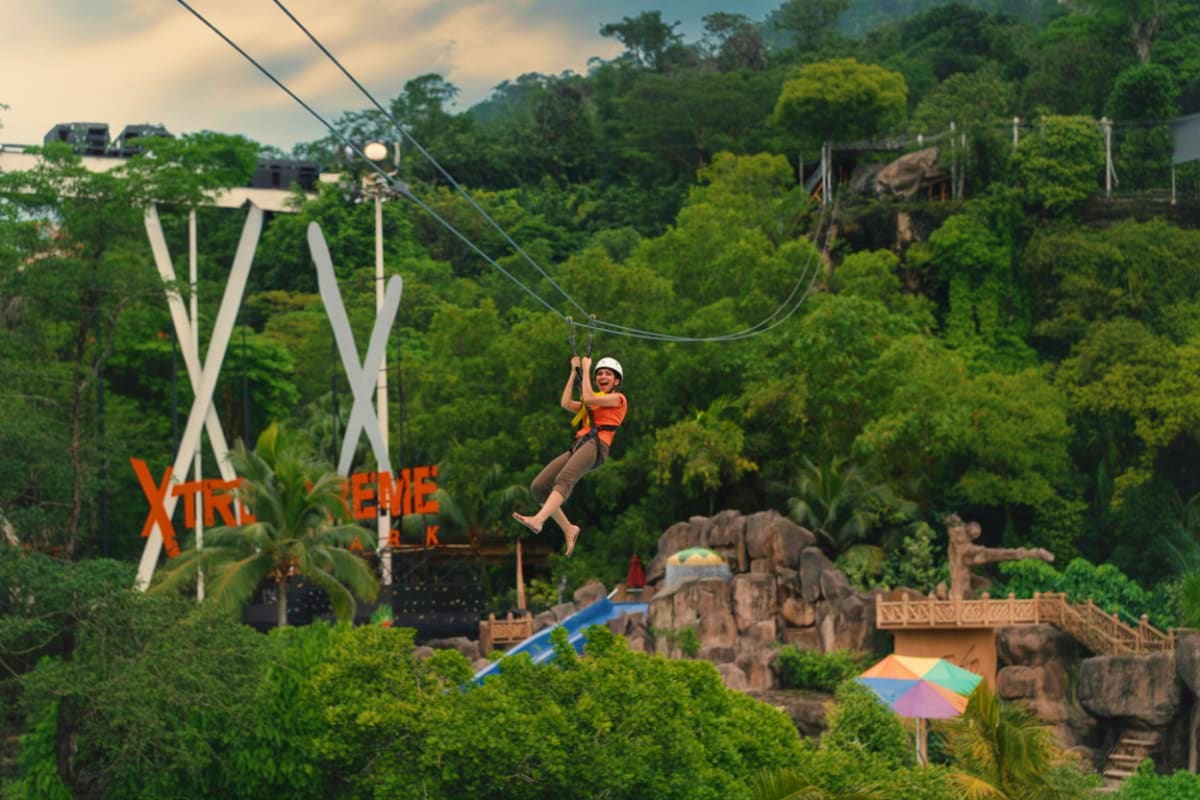 Person ziplining over tropical forest at Sunway Lagoon adventure park with ancient temple ruins below
