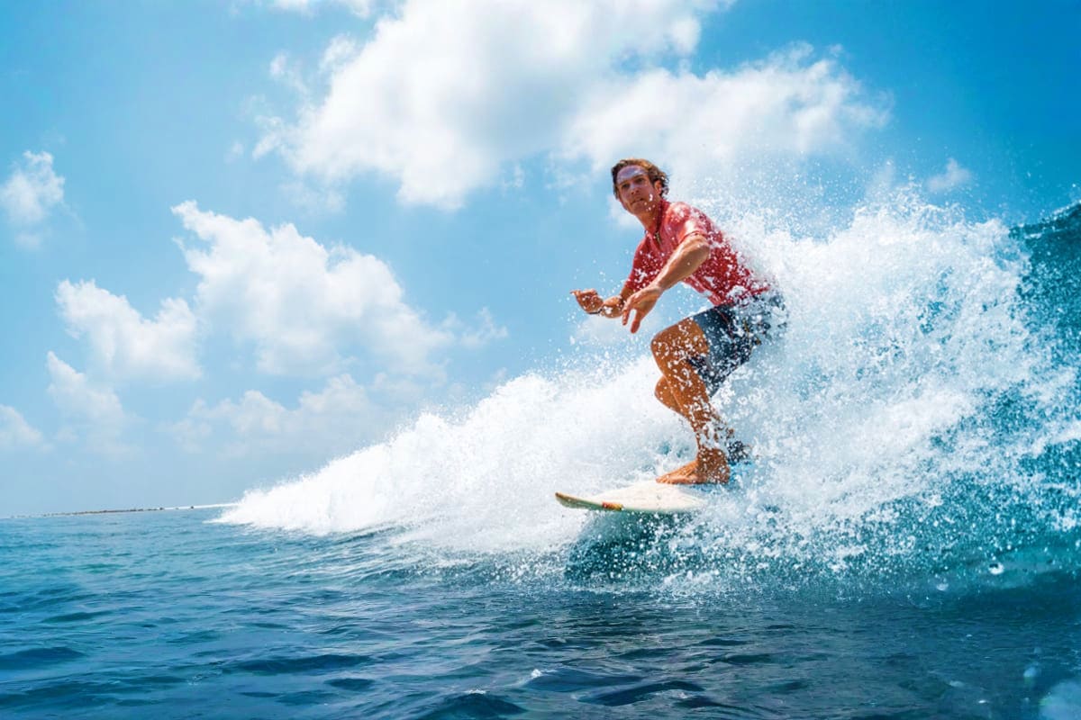 Surf High Experience in Dubai Man surfing on a large wave in clear turquoise ocean water under blue sky with white clouds