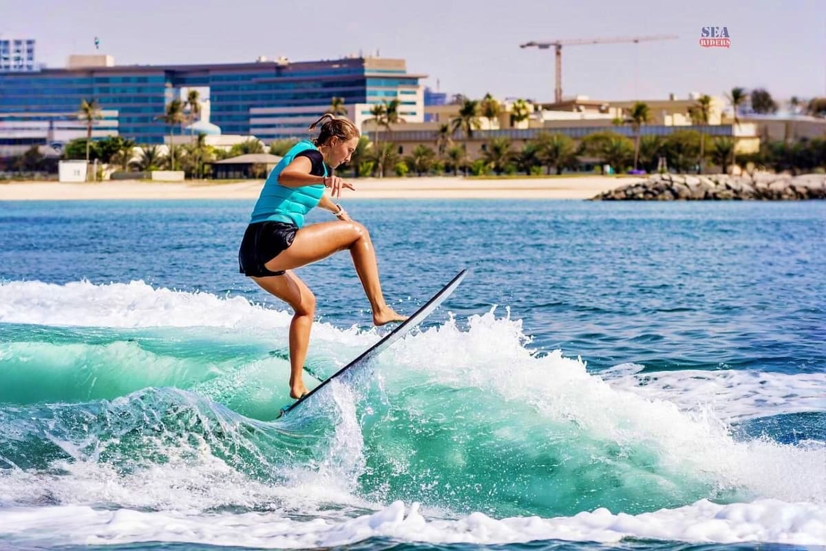 Surf High Experience in Dubai Female surfer riding a wave in turquoise water with Dubai beach and waterfront hotels in the background