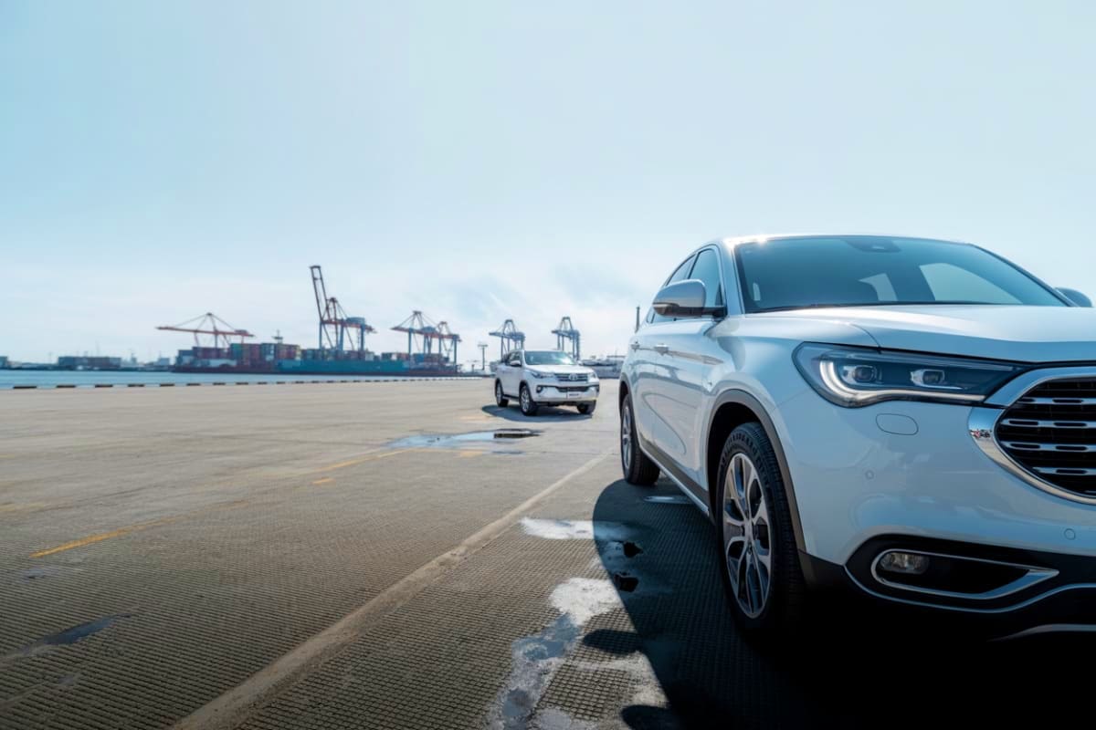 White SUVs parked at a cargo port with shipping containers and cranes in the background, representing airport transfer servic