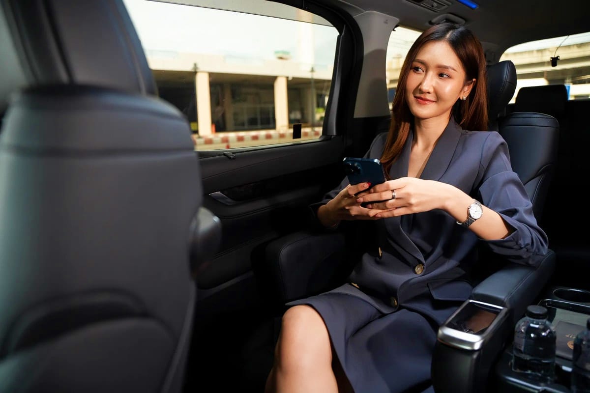 Professional woman in business suit sitting in car backseat holding smartphone during airport transfer service