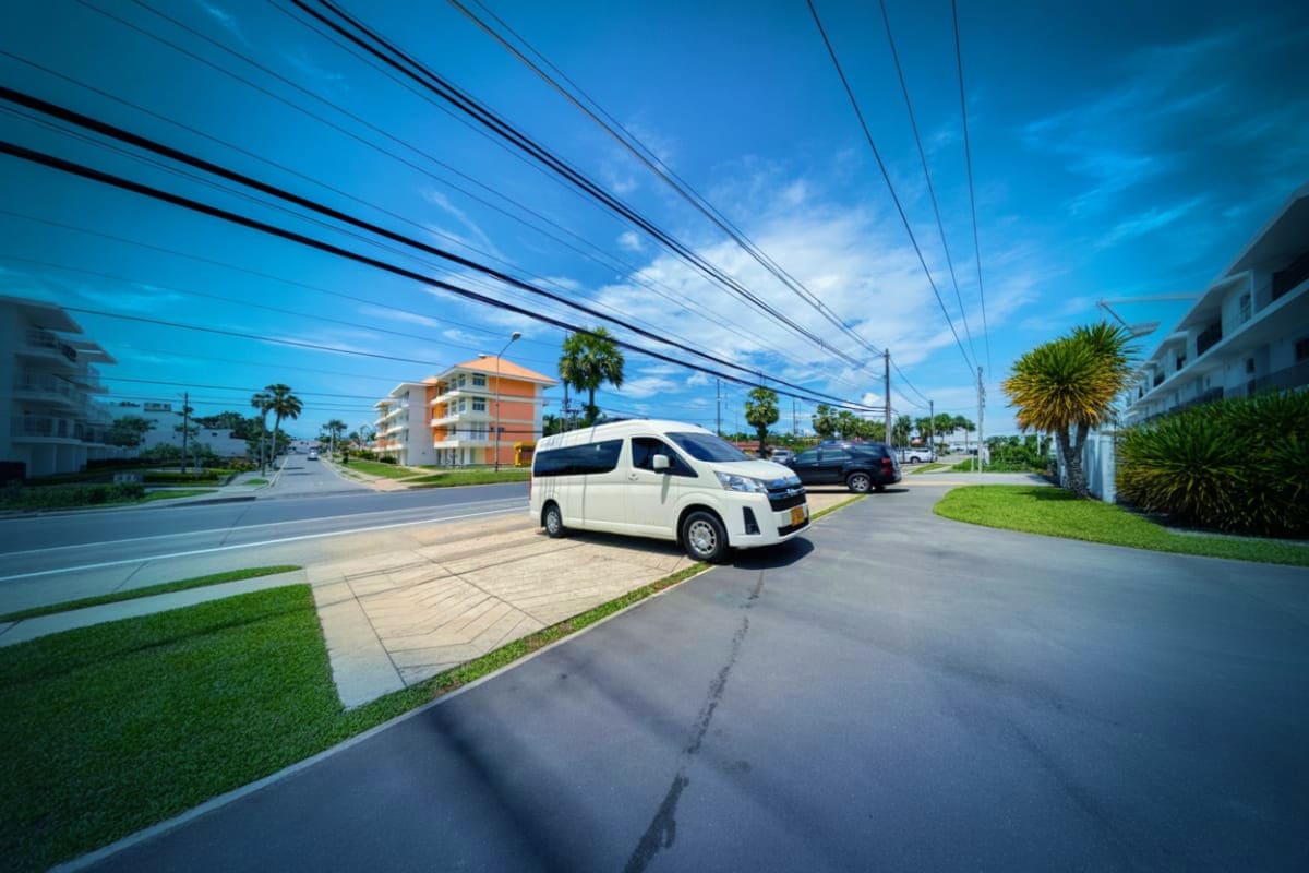White minivan parked on residential street with palm trees, apartment buildings, and power lines under blue sky