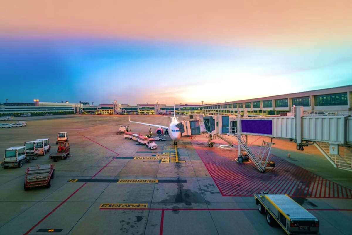 Commercial airplane docked at airport gate during sunset with ground service vehicles and boarding bridge at Suvarnabhumi Air